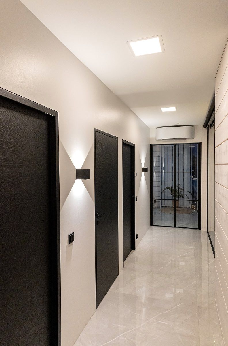 Il corridoio è illuminato in modo uniforme dalle plafoniere Paneeli 300 e dalle applique FUNK nere, con un'intensa illuminazione verde verso l'alto e verso il basso.